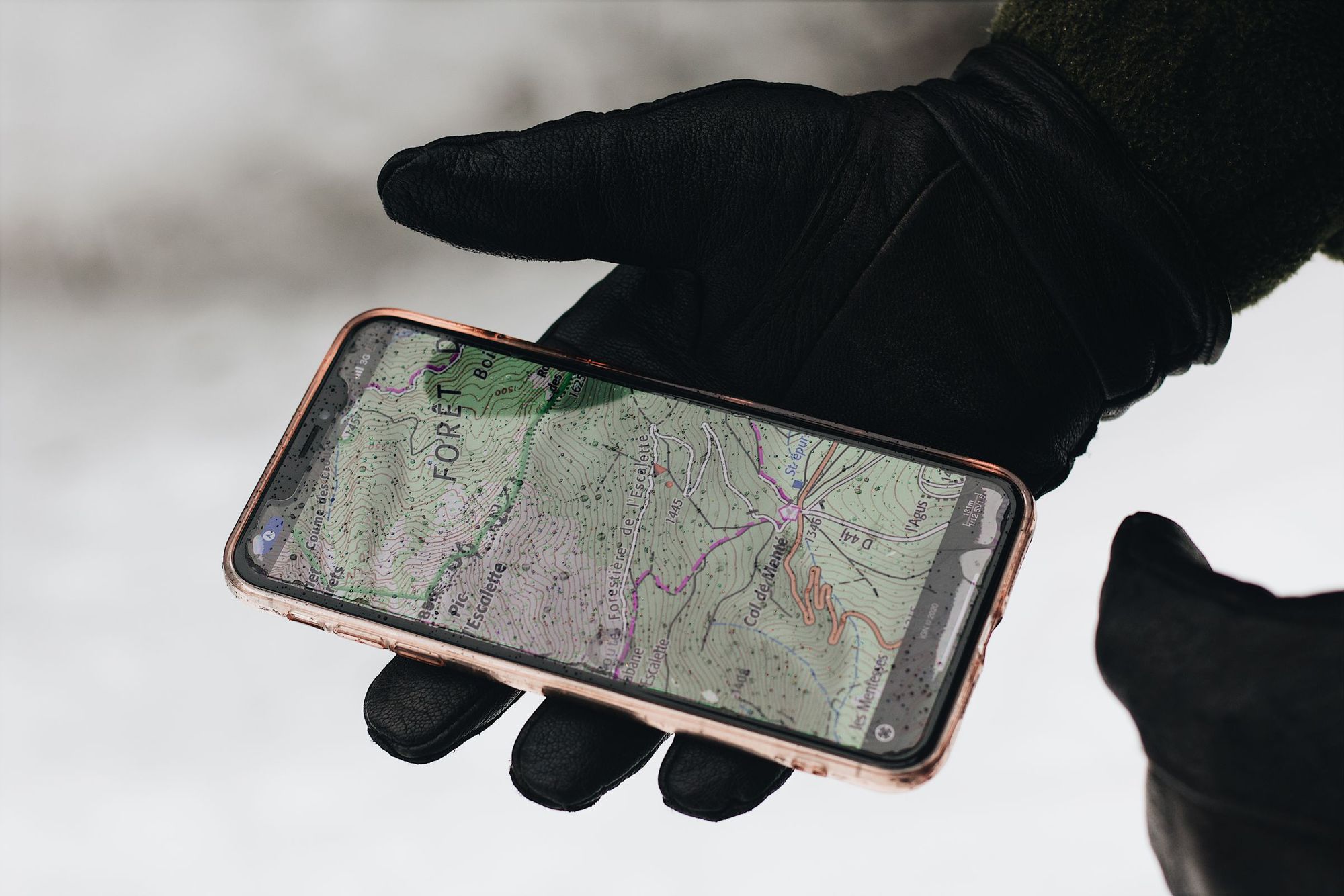 A gloved hand holding a phone with a map open, outdoors on a job site.